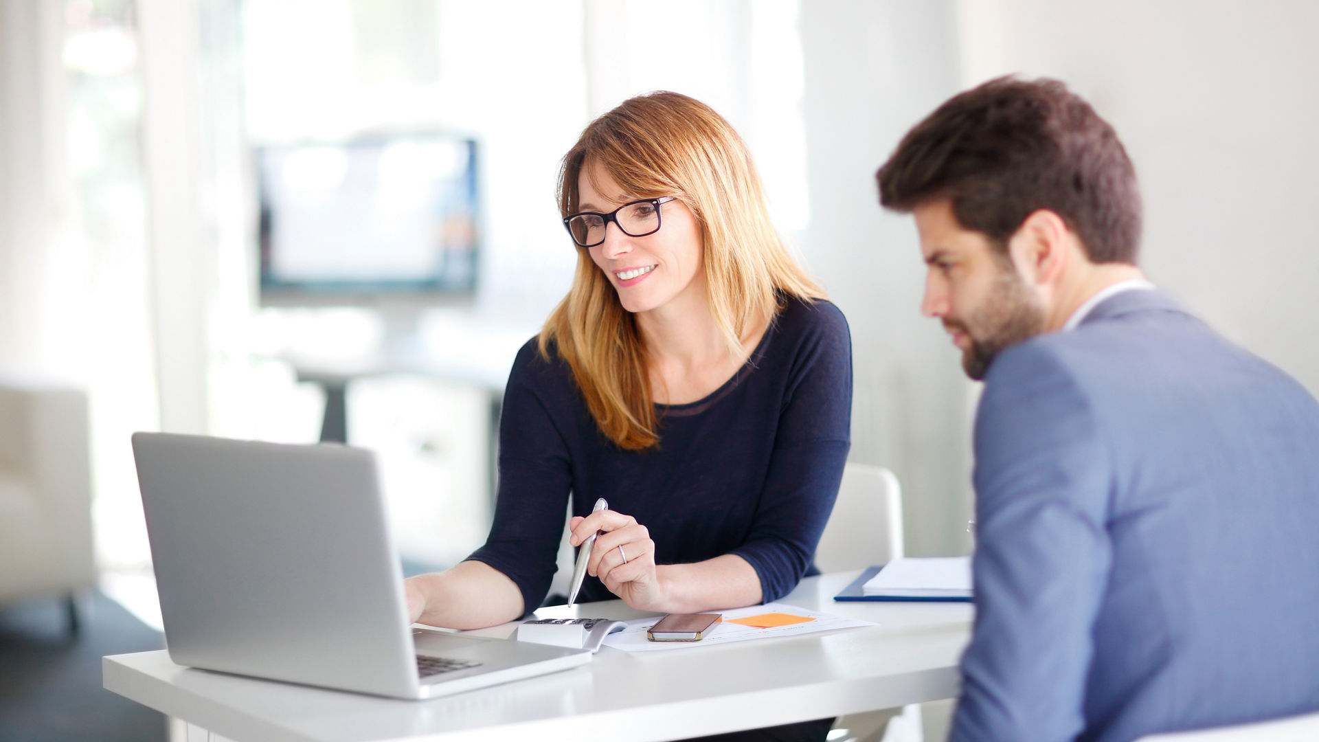 Portrait of investment advisor businesswoman sitting at office in front of computer and consulting with young professional man. 