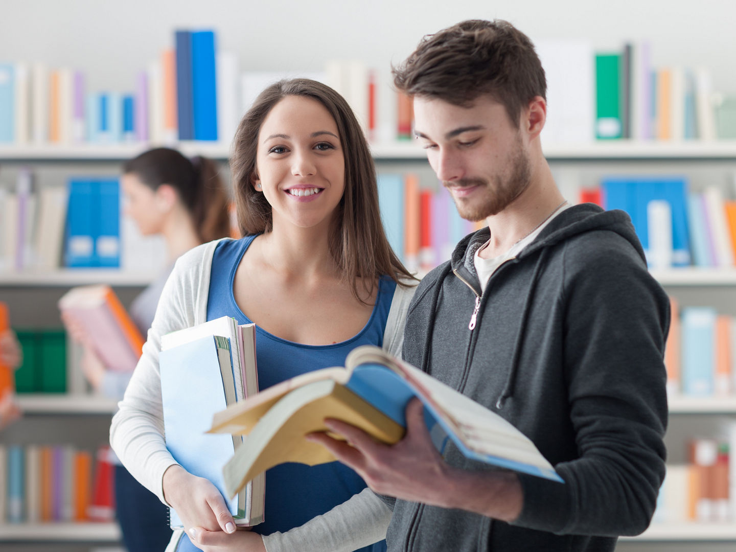 Happy smiling students in the school library, they are holding books and studying together, friendship and learning concept