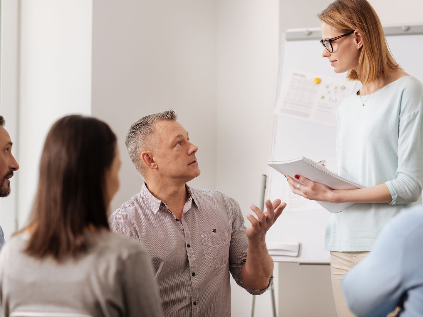 Take an order. Attractive woman listening attentively to her colleague standing in semi position, holding notebook