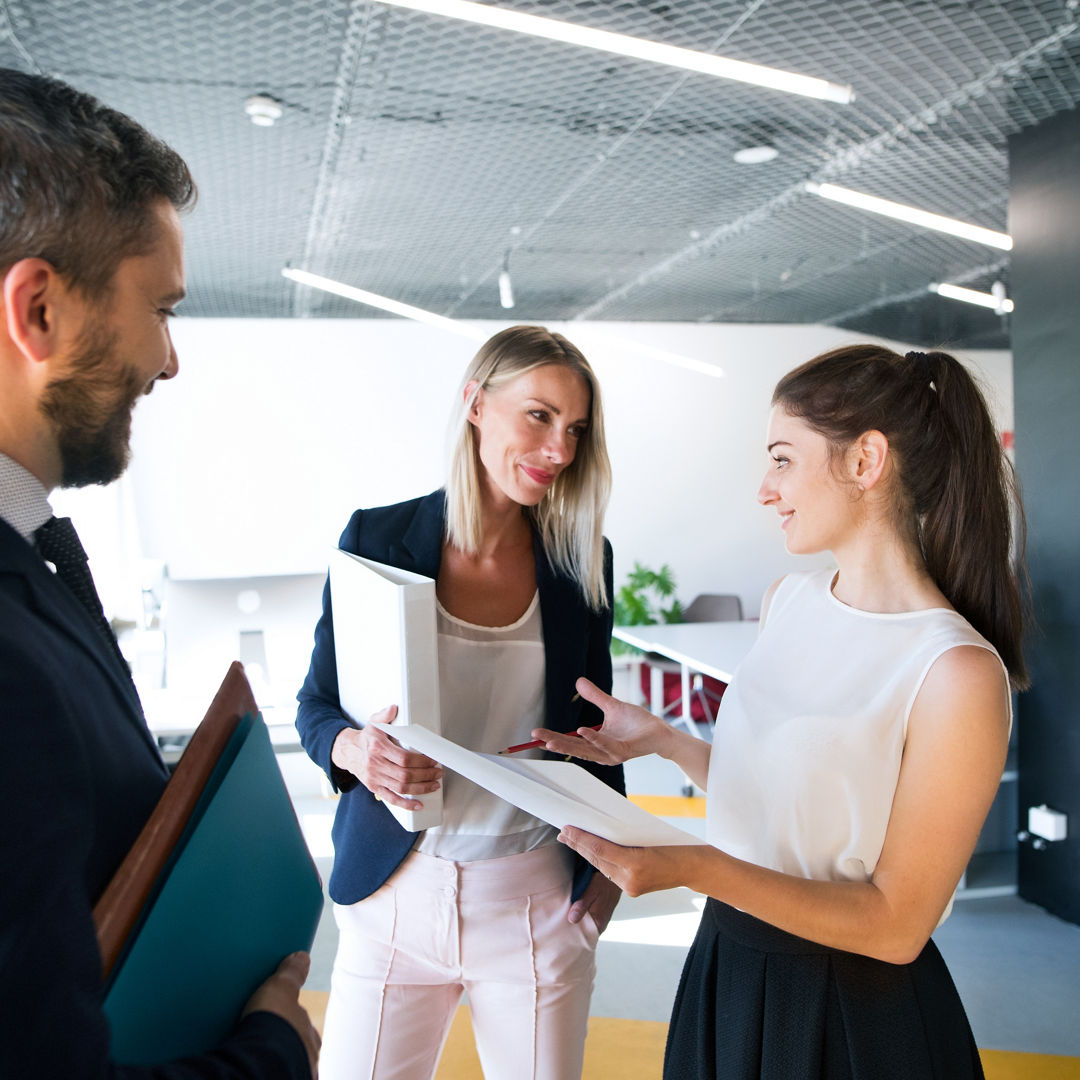 Three business people in the workplace. Two women and man standing in the office talking together.