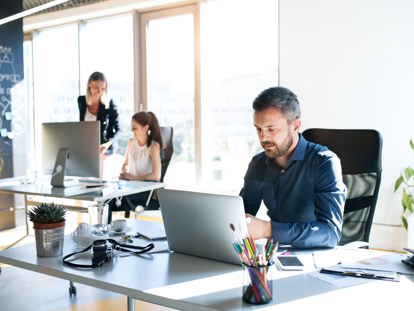 Three business people in the workplace. Two women and man sitting in the office working together.