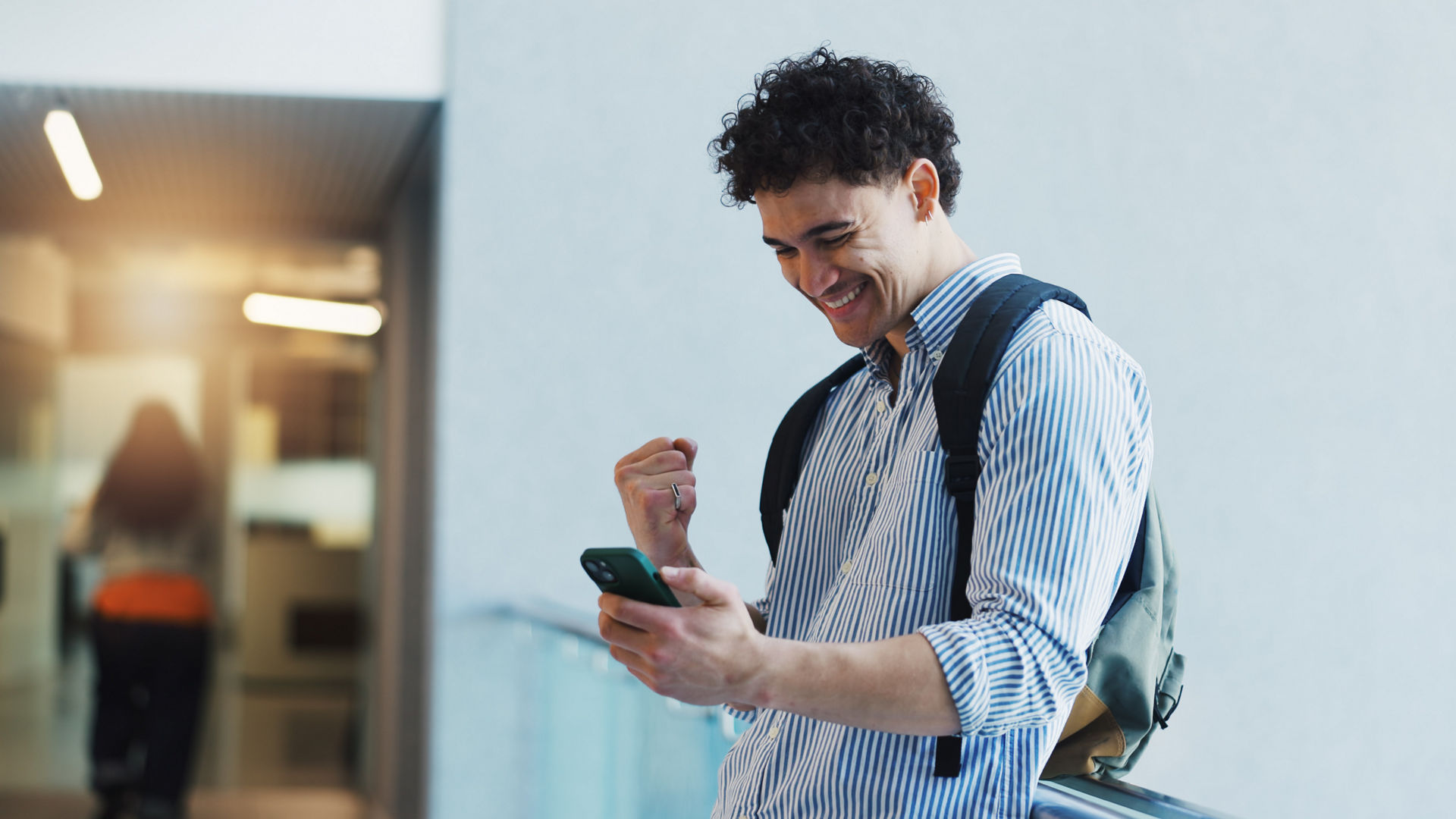 Education, fist pump and phone with student man in university hallway as scholarship winner. App, celebration and success with happy learner on college campus for good news of school bursary award.