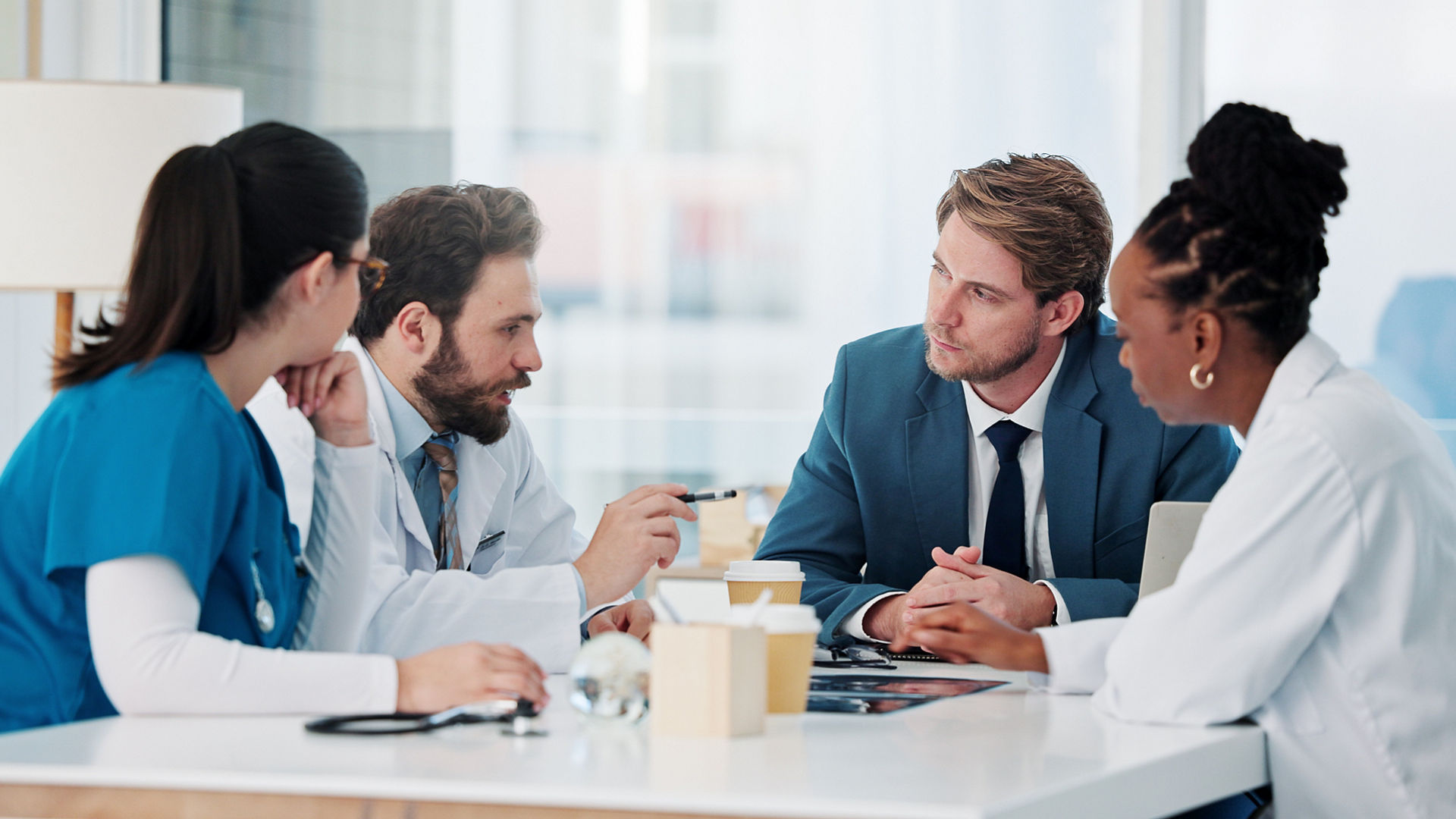 Businessman, doctors and nurse with meeting in hospital for research grant, vaccine trial or planning. Healthcare, people or staff with update on medical funding, investment opportunity or discussion.