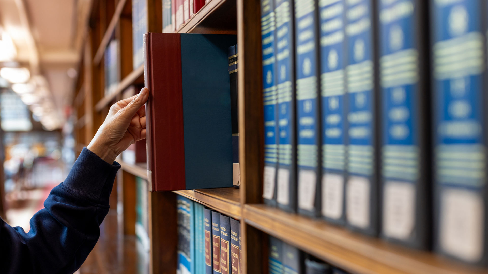 Hand selecting book from wooden library shelf. Legal research concept, attorney reference material, system study, academic knowledge and professional legislation archive.