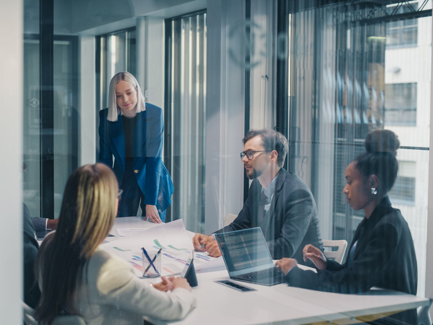 Business Manager Leads a Focused Planning Meeting in a Glass Office, Guiding a Diverse Team as They Review Reports, Discuss Strategy, Analyze Performance Metrics, Share Ideas