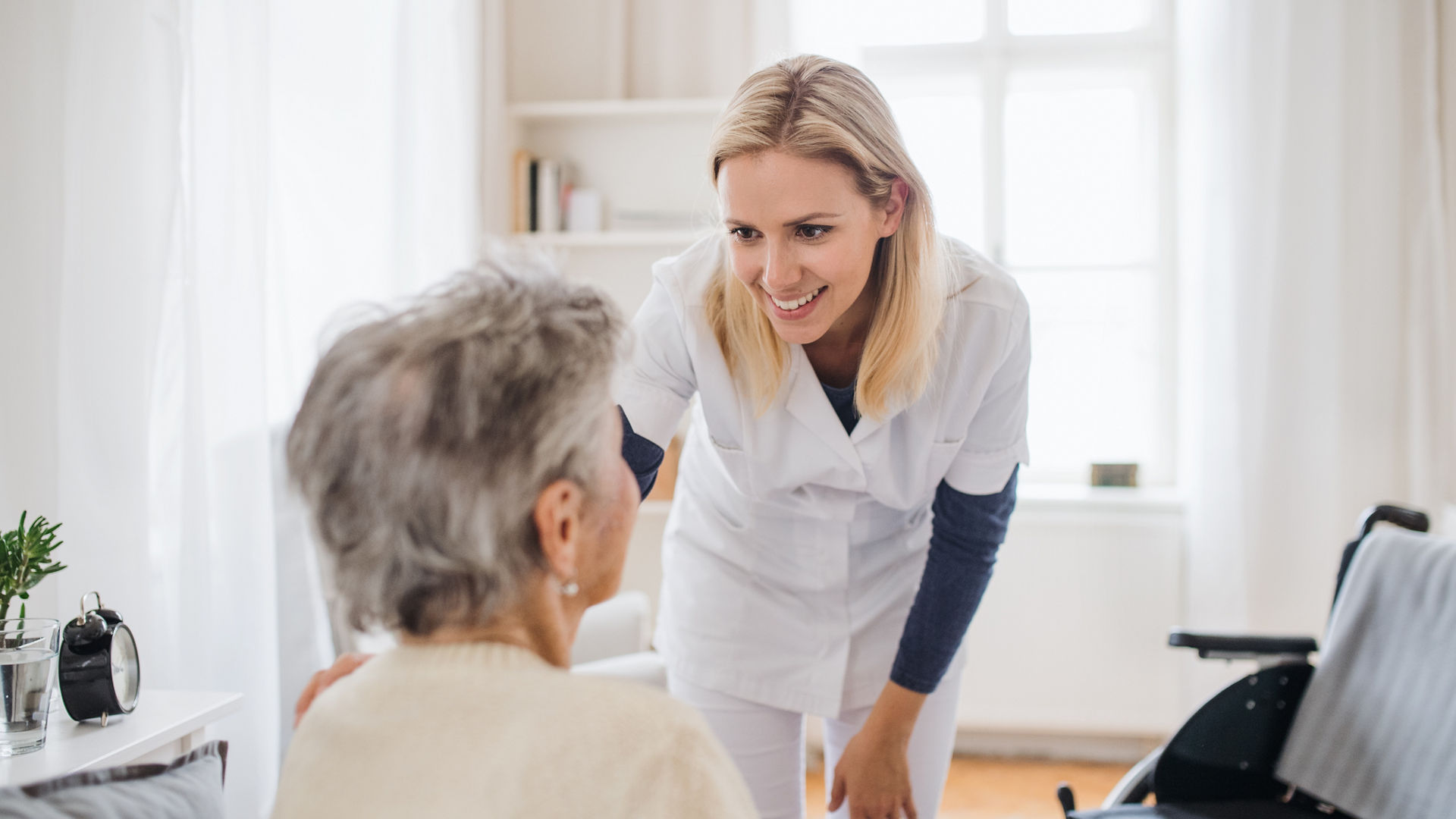 A health visitor talking to an unrecognizable senior woman sitting on bed at home.