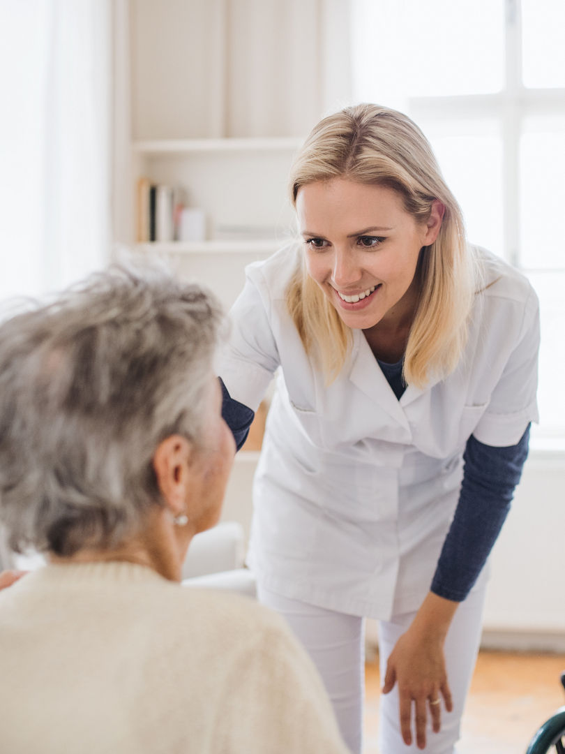 A health visitor talking to an unrecognizable senior woman sitting on bed at home.