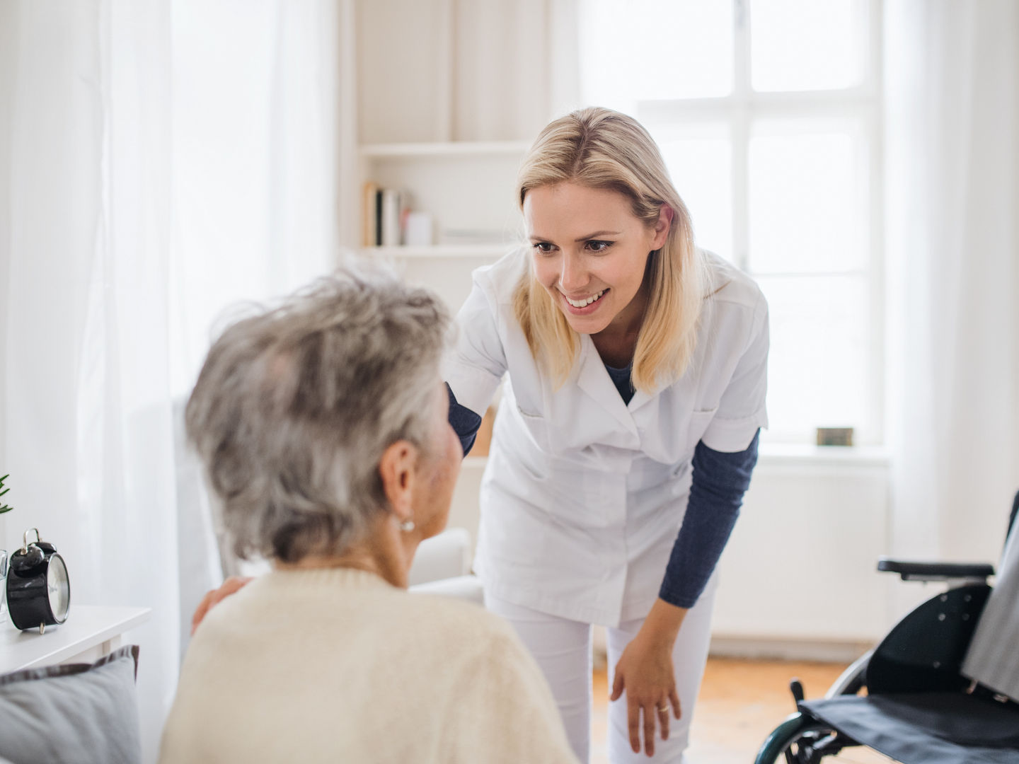 A health visitor talking to an unrecognizable senior woman sitting on bed at home.
