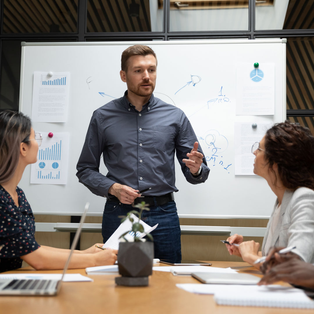 Confident businessman executive mentor ceo leader talk to employees group during corporate briefing in boardroom, serious male boss explain work plan to multiethnic workers at office meeting table