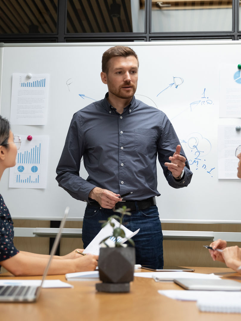 Confident businessman executive mentor ceo leader talk to employees group during corporate briefing in boardroom, serious male boss explain work plan to multiethnic workers at office meeting table