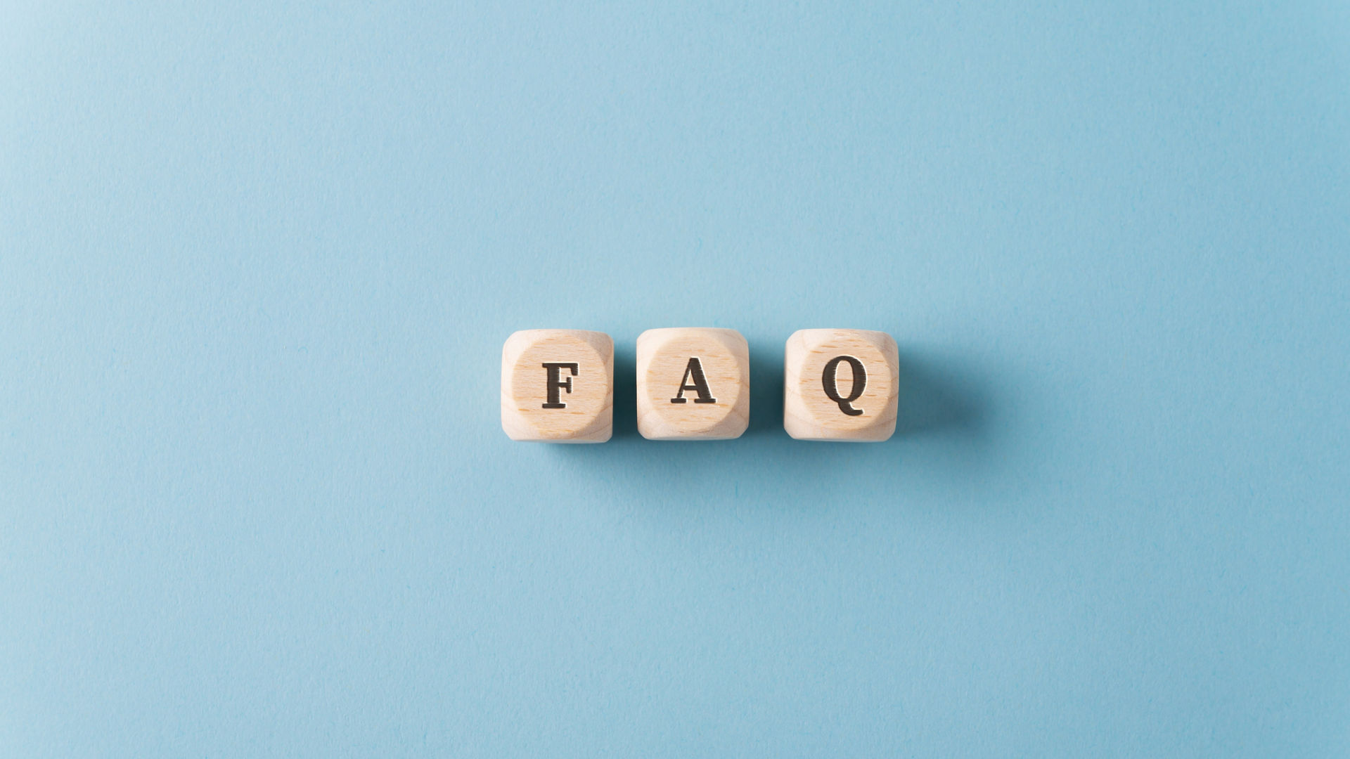 Three wooden dices spelling FAQ over light blue background.