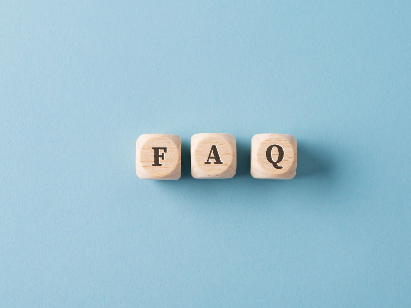 Three wooden dices spelling FAQ over light blue background.