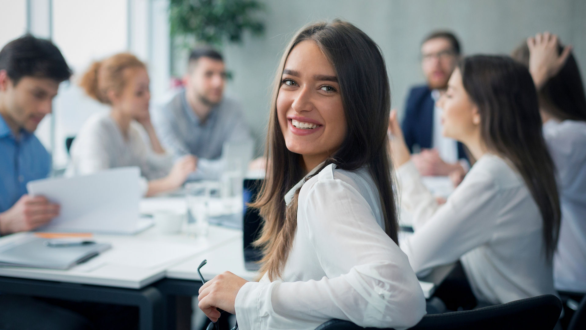 Positive secretary smiling to camera during meeting with colleagues working on background