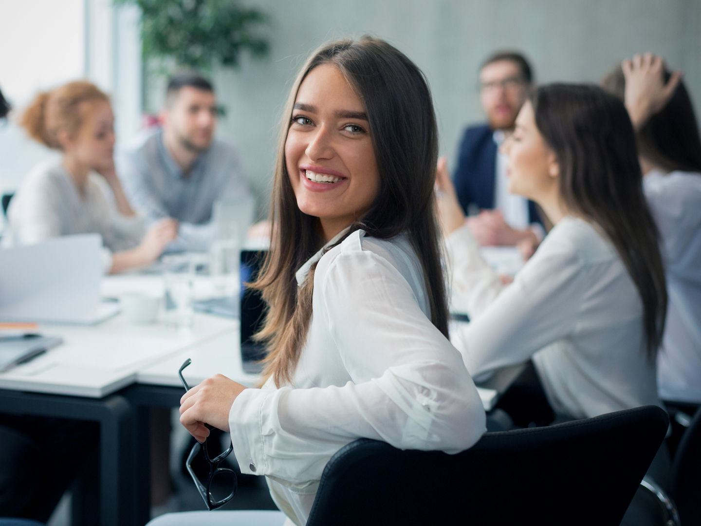 Positive secretary smiling to camera during meeting with colleagues working on background