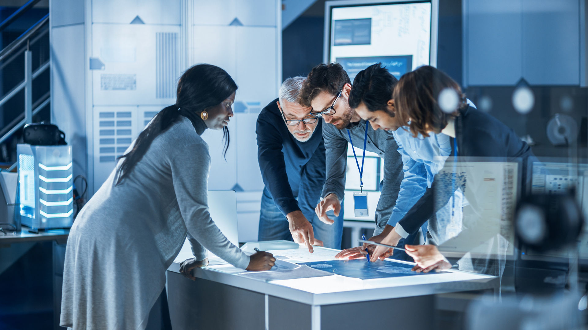 Engineers Meeting in Technology Research Laboratory: Engineers, Scientists and Developers Gathered Around Illuminated Conference Table, Talking and Finding Solution, Inspecting and Analysing Industrial Engine Design.