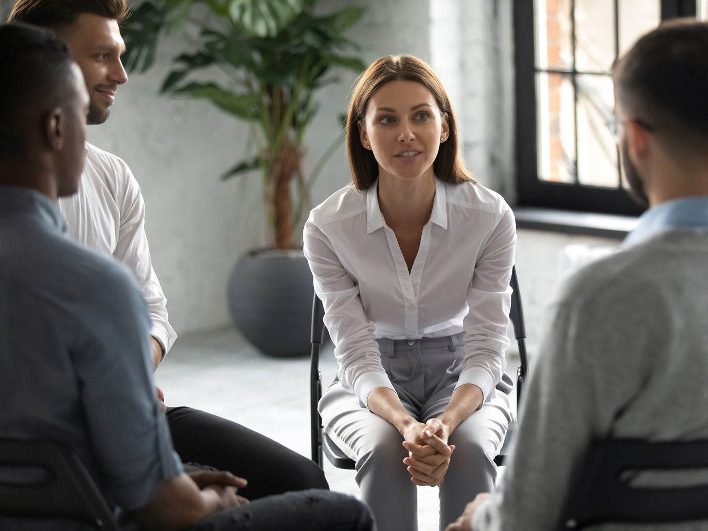 Smiling attractive female psychologist counselling speaking with diverse people sitting in circle at group therapy session. Business coach training staff, having fun, team building activity at work.