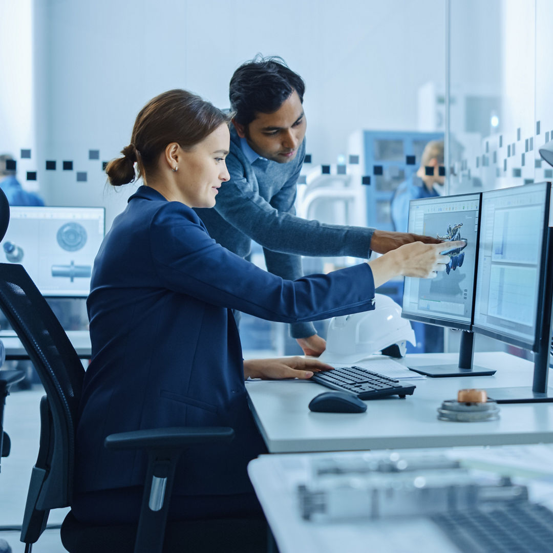 Inside Factory Office: Male Project Supervisor Talks to a Female Industrial Engineer who Works on Computer, Talk. In Workshop: Professional Workers Use High-Tech Industry 4 CNC Machinery, Robot Arm.