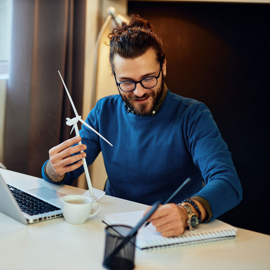 Attractive bearded environmentalist sitting in his office and drawing new windmill model.