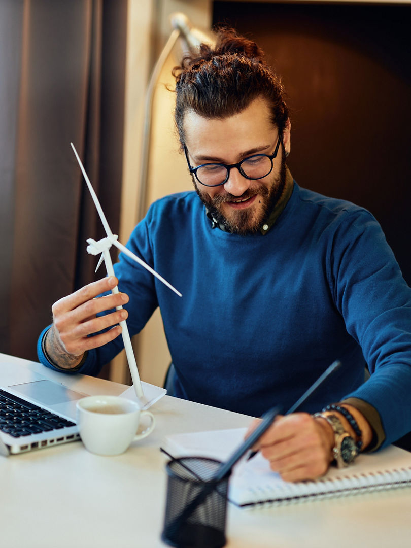 Attractive bearded environmentalist sitting in his office and drawing new windmill model.