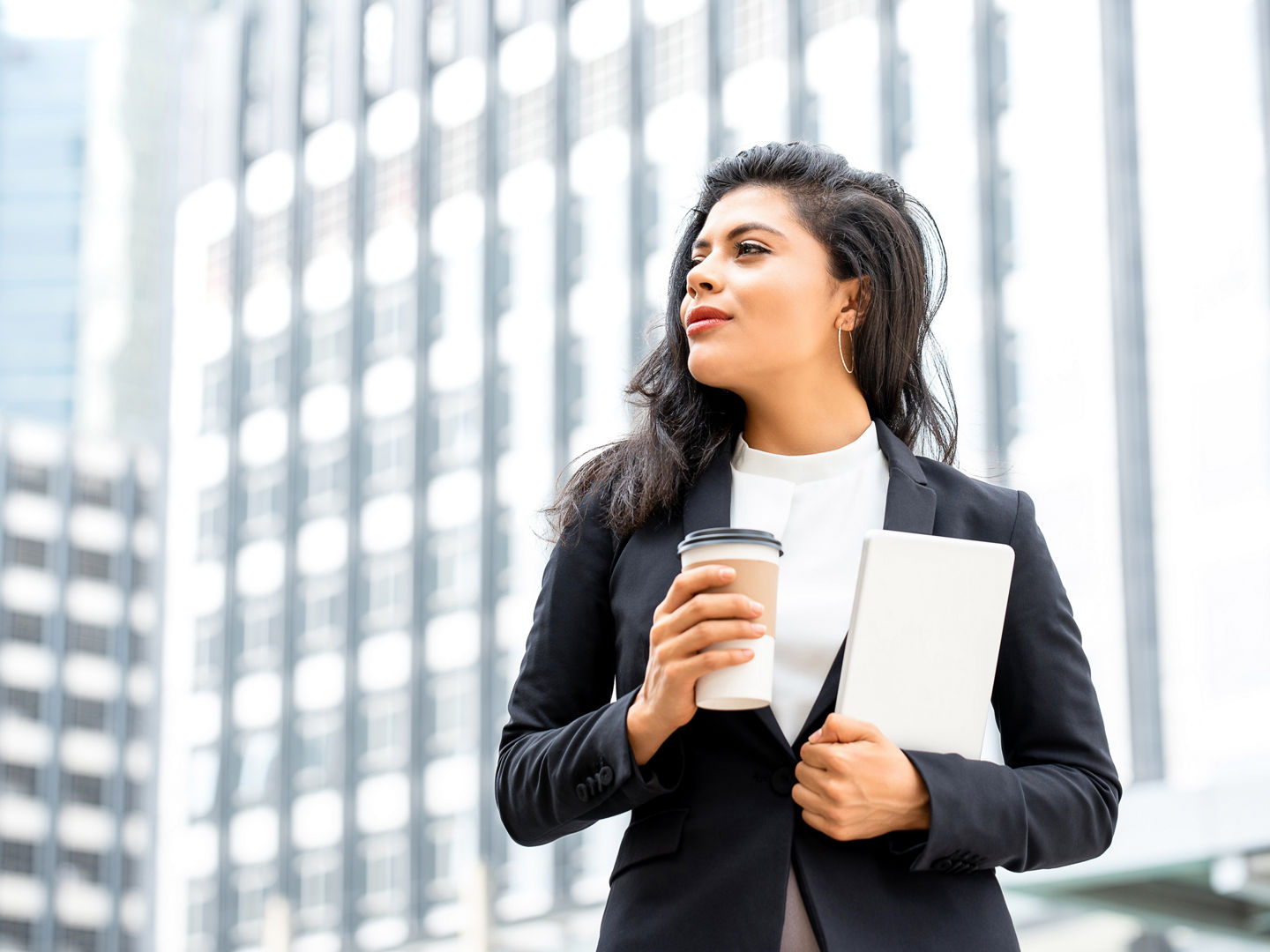 Portrait of beautiful young confident Hispanic businesswoman taking a coffee break holding tablet in urban city background