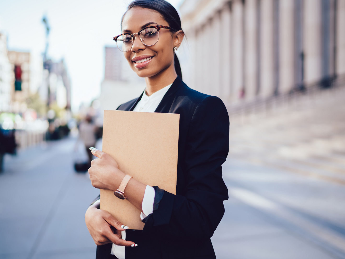Portrait of successful african american student of faculty of law with folder in hands smiling at camera.Cheerful female office worker with dark skin dressed in formal wear standing outdoors