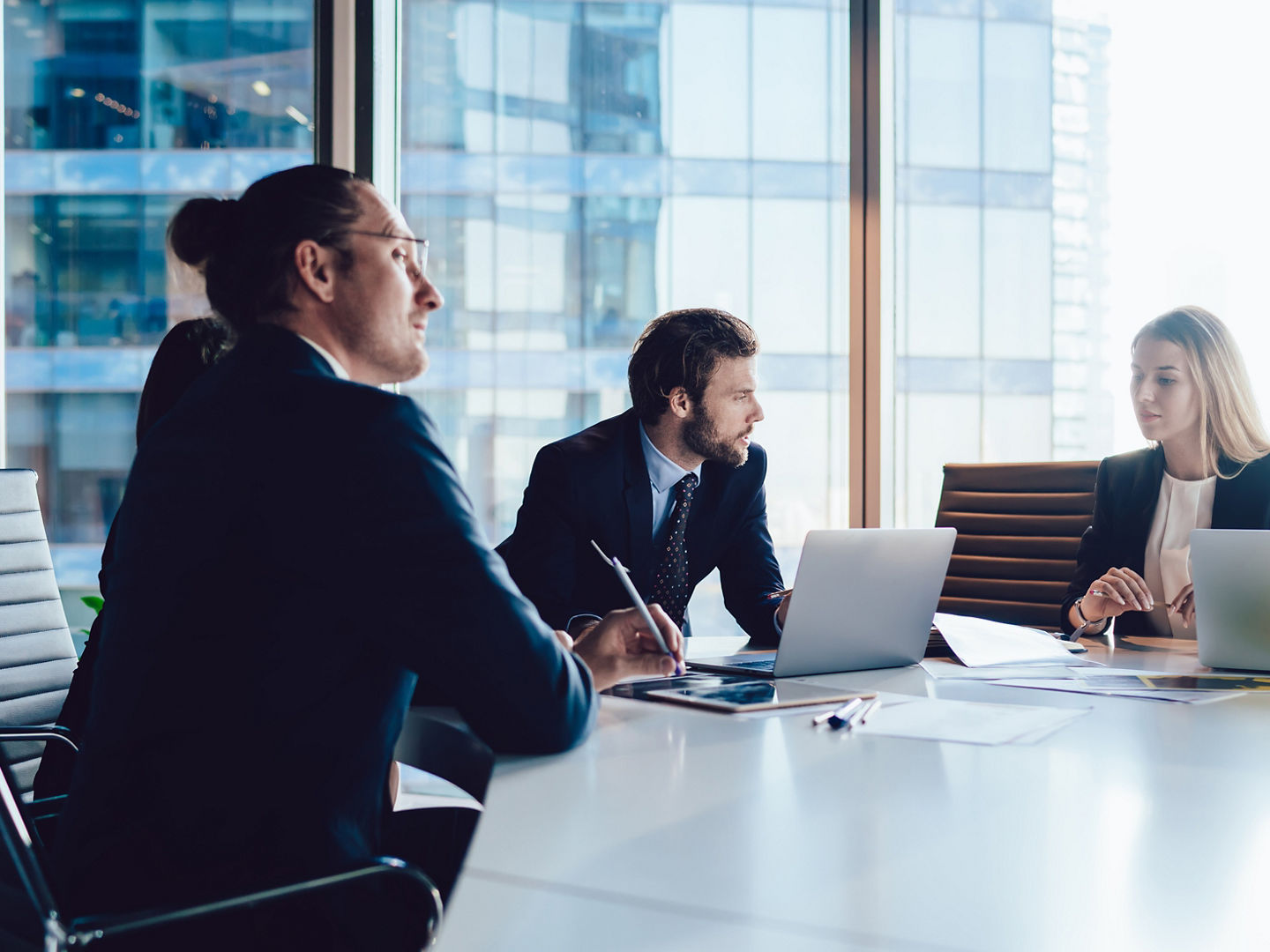 Group of focused smart male and female coworkers gathering at table in spacious office and working on laptop while creating new project