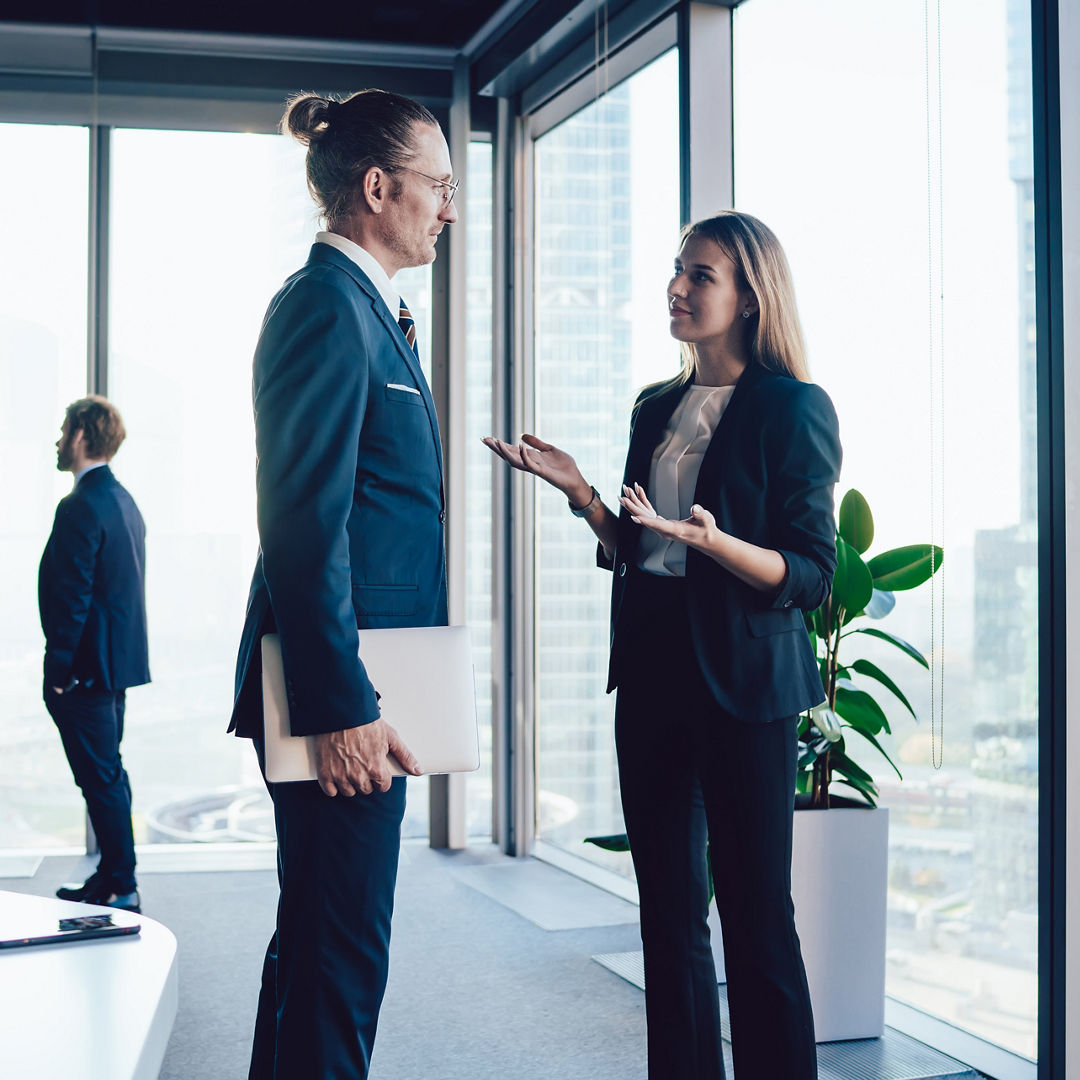 Side view of coworking man and woman in formal clothing talking about new project during meeting with colleagues while standing in modern office and looking at each other