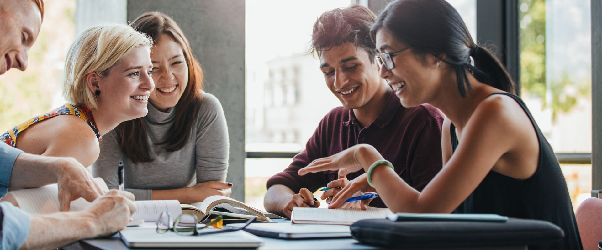 Happy young university students studying with books in library. Group of multiracial people in college library.