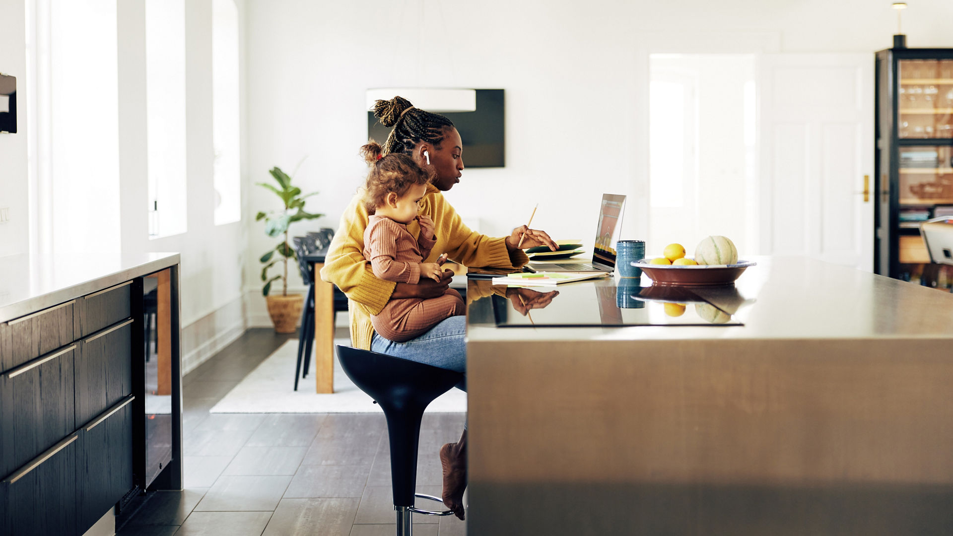 Young African mother working online from home on a laptop with her little daughter sitting on her lap