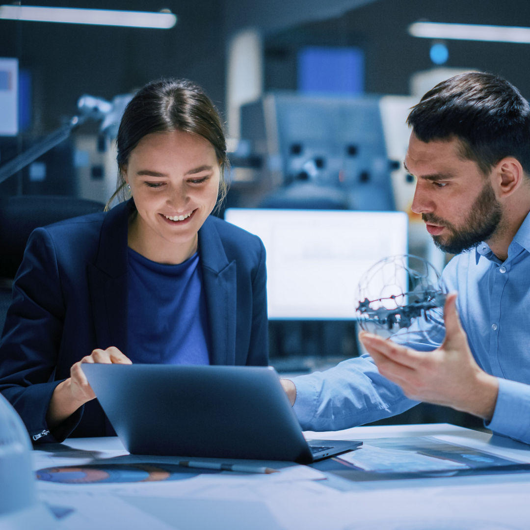 Industry 4.0 Modern Factory Meeting Room: Chief Engineer Holds Mechanism, Shows it to Female Designer, They Talk. Scientists in Contemporary Lab Build Electronic Machinery for With Futuristic Design