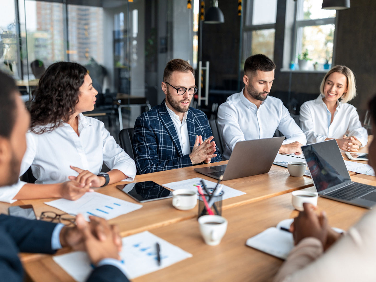 Brainstorming And Teamwork. Businessman Presenting Startup Idea To Diverse Coworkers During Corporate Meeting, Sitting At One Desk In Modern Office. Selective Focus