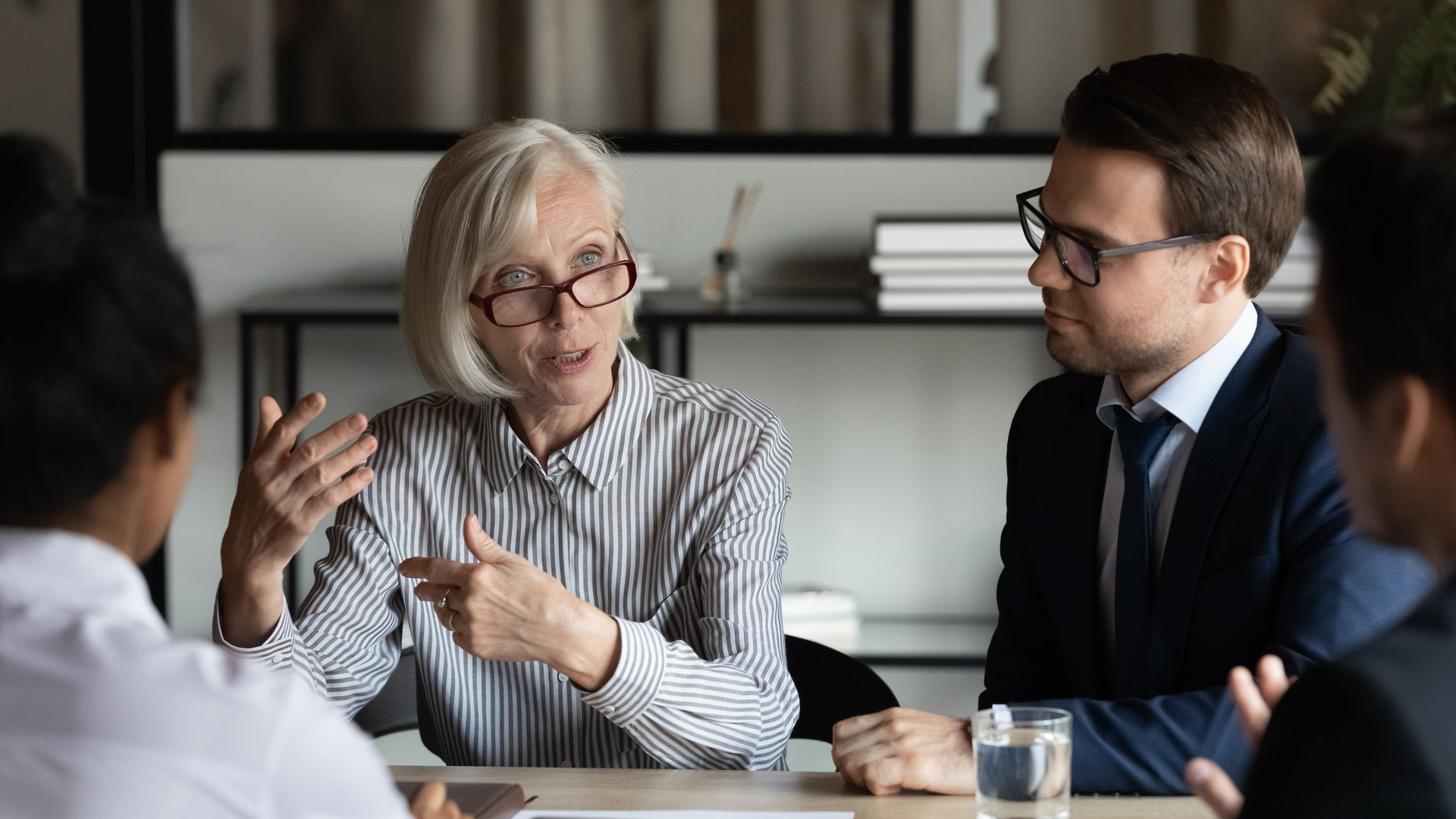 Middle aged mature mentor training interns, corporate coach teaching staff, teacher explaining work process to new employees. Female business leader speaking at meeting, conference, briefing