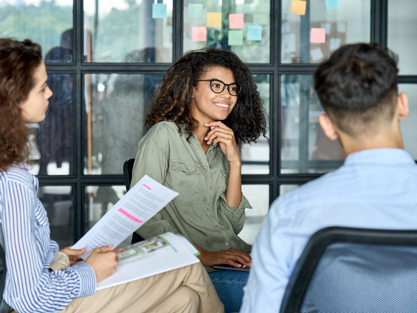 Happy young African American woman brainstorming marketing ideas about project strategy among diverse multiracial coworkers, business startup creative team or students group in office holding papers.