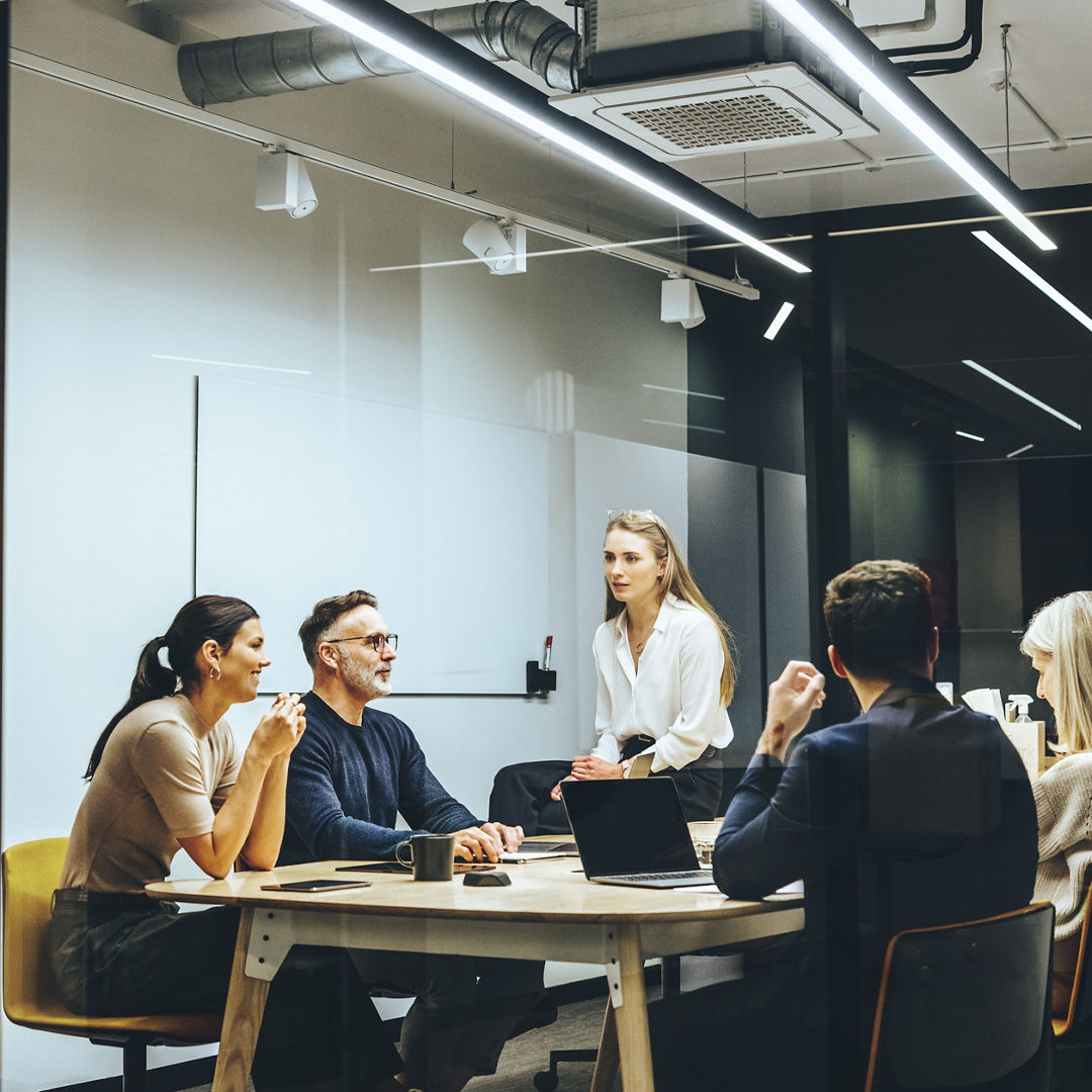 Group of colleagues having a meeting in a transparent boardroom. Team of diverse business professionals having a discussion during a briefing. Businesspeople collaborating on a new project.