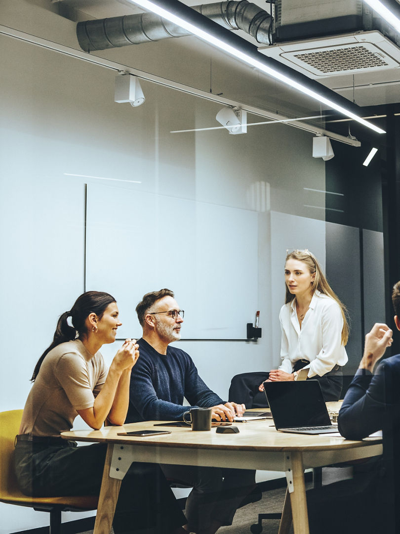 Group of colleagues having a meeting in a transparent boardroom. Team of diverse business professionals having a discussion during a briefing. Businesspeople collaborating on a new project.