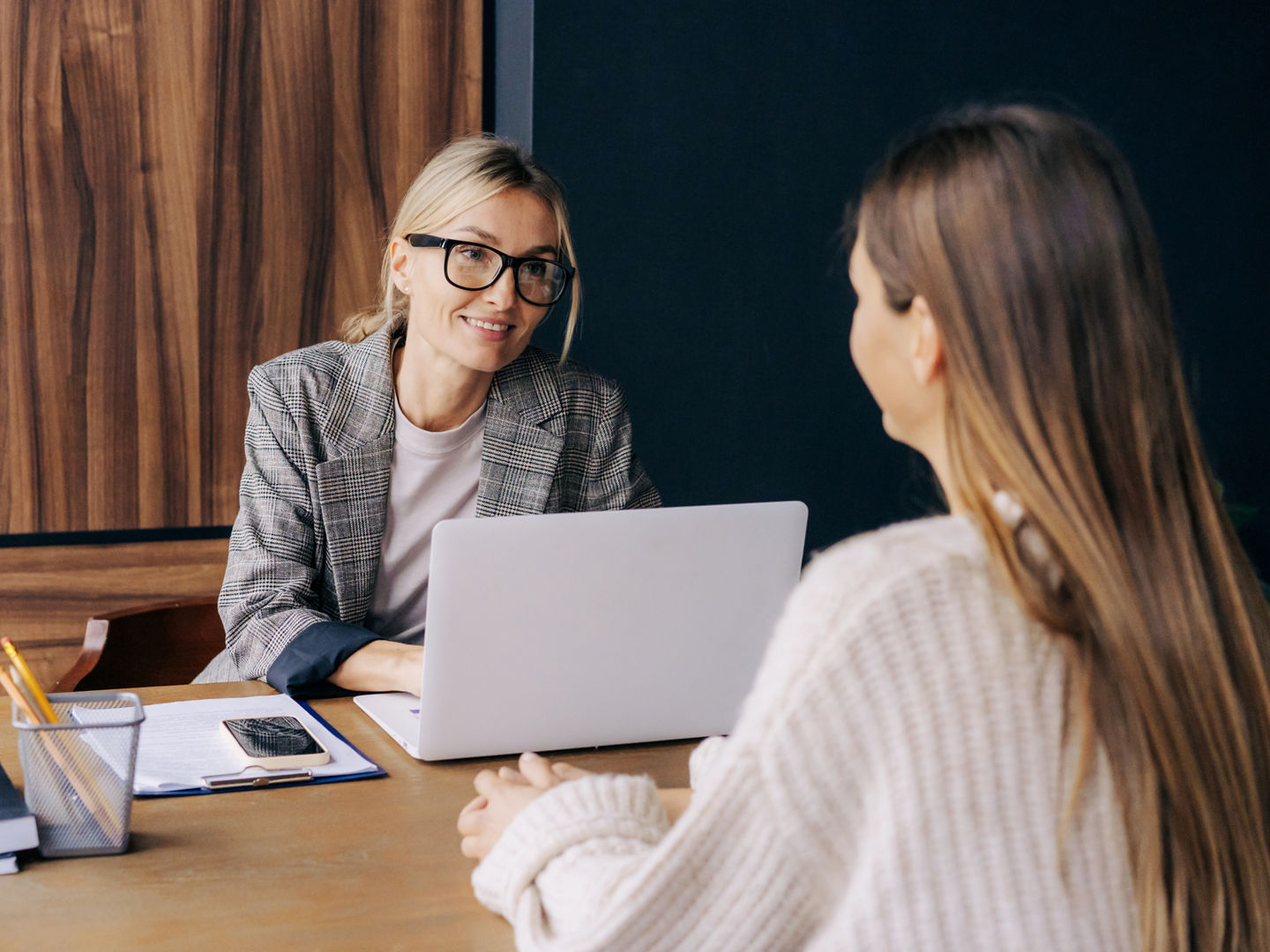 A female professional sitting at a desk in an office is interviewing a candidate for a position.