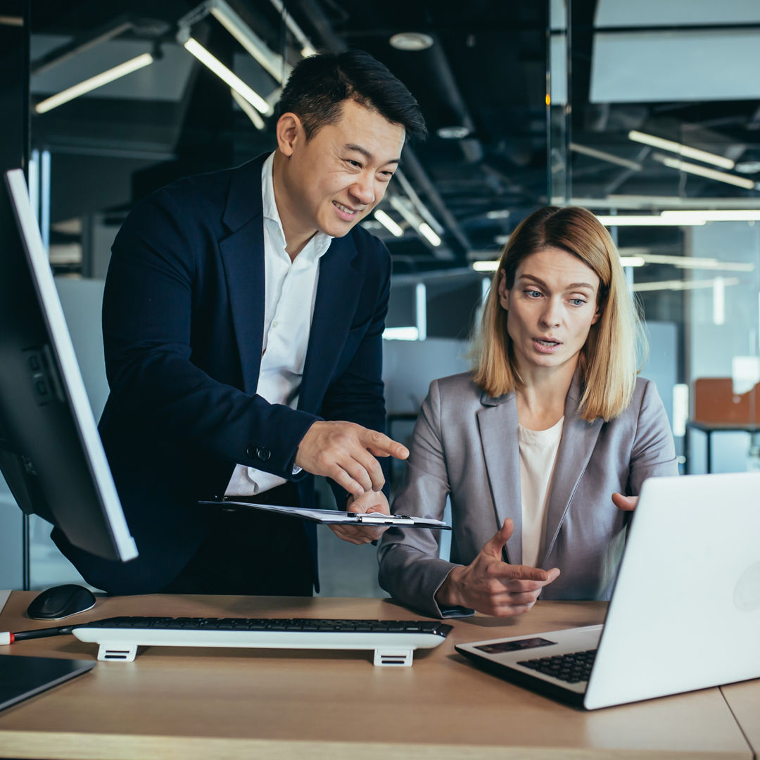 two business people consulting on a project looking at computer monitor screen sitting in the office. Asian male employee Coworker explains colleagues ideas and strategies accountant, financial report