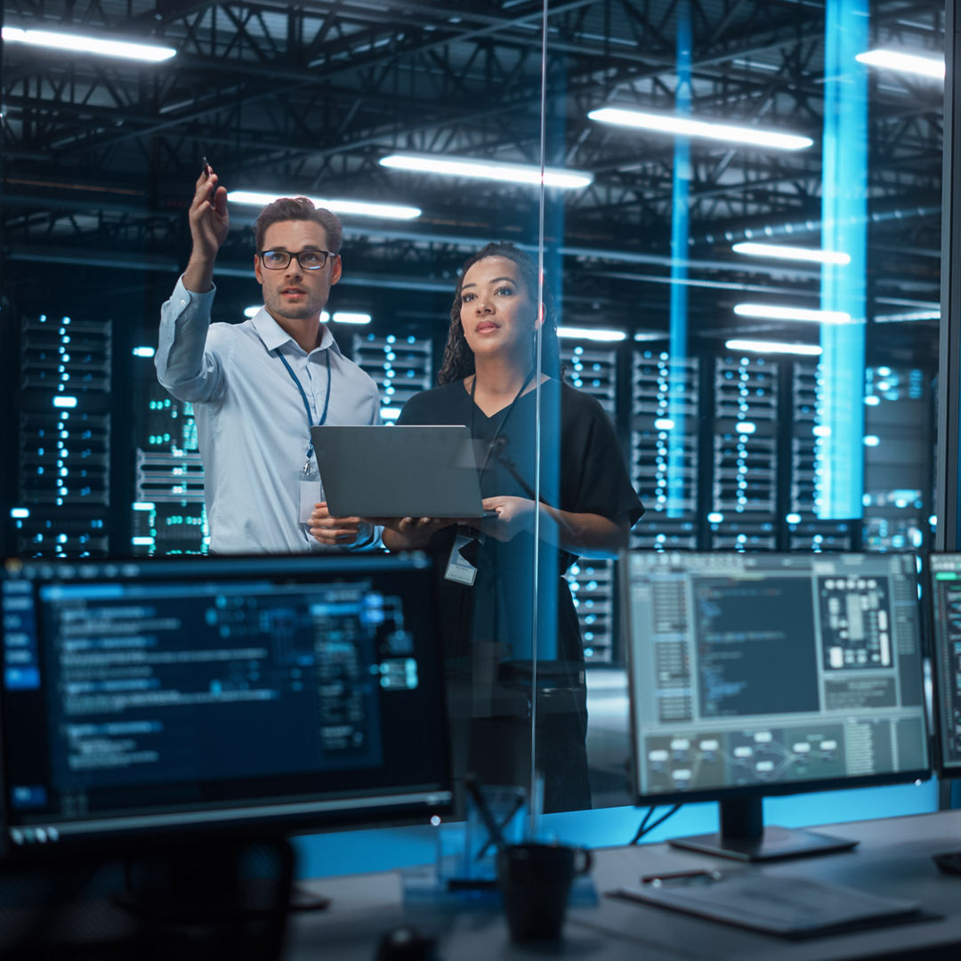 Successful Corporate Top CEO's Talking, Using Laptop Computer Standing in Big City Office at Night. Two Successful Managers Discuss Environmental, Social, Corporate Governance for e-Commerce Project