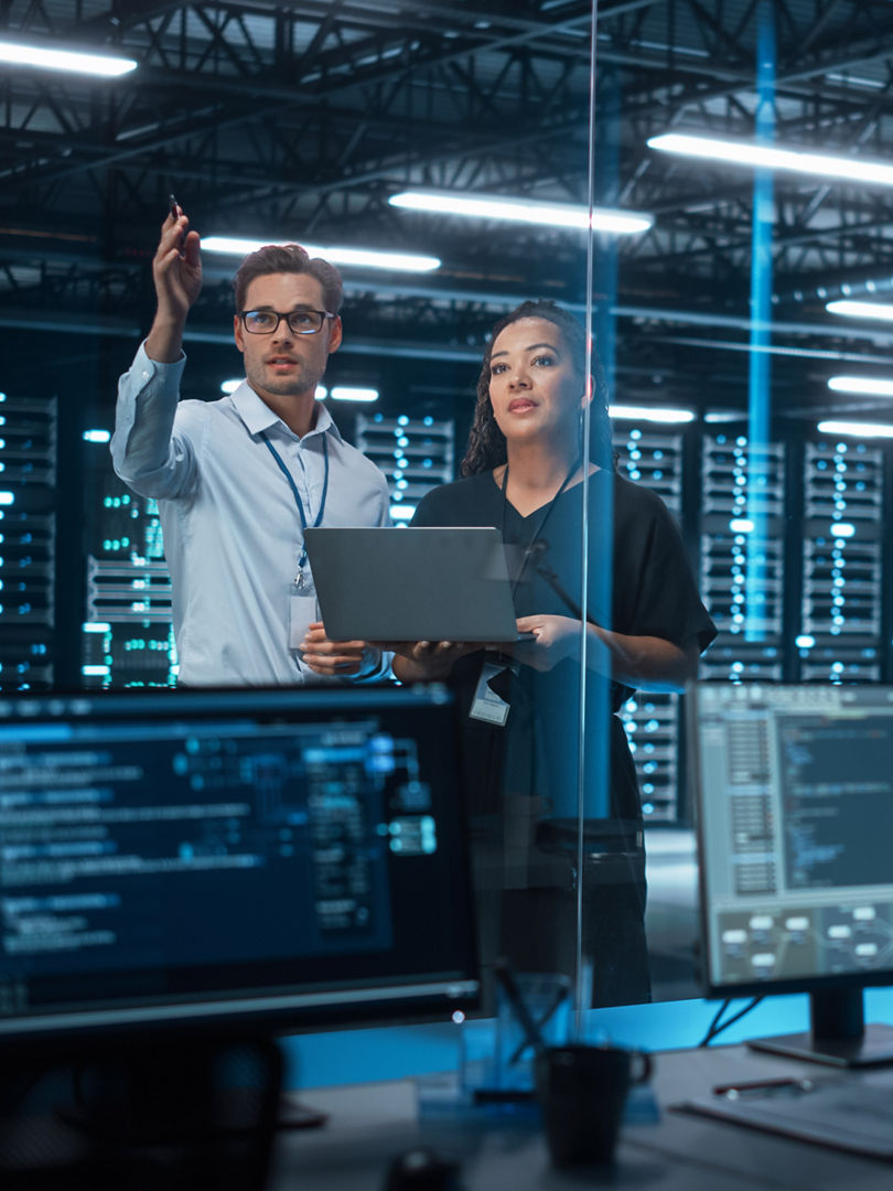 Successful Corporate Top CEO's Talking, Using Laptop Computer Standing in Big City Office at Night. Two Successful Managers Discuss Environmental, Social, Corporate Governance for e-Commerce Project