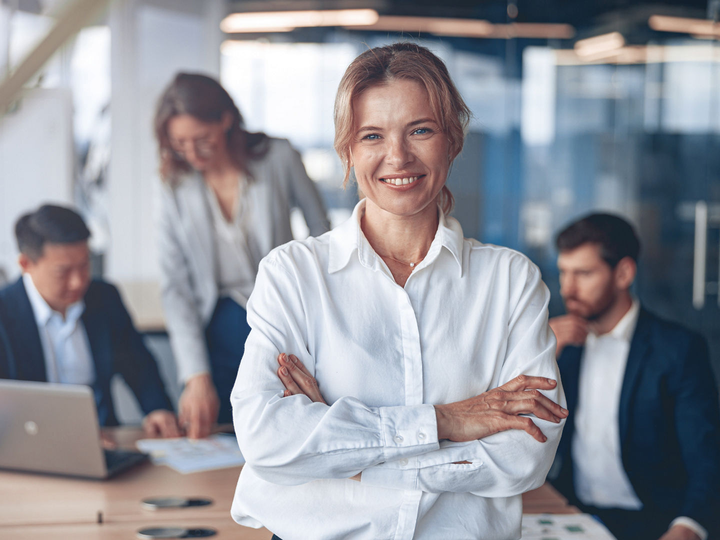 Portrait of beautiful smiling mature businesswoman with her colleagues on background in office.