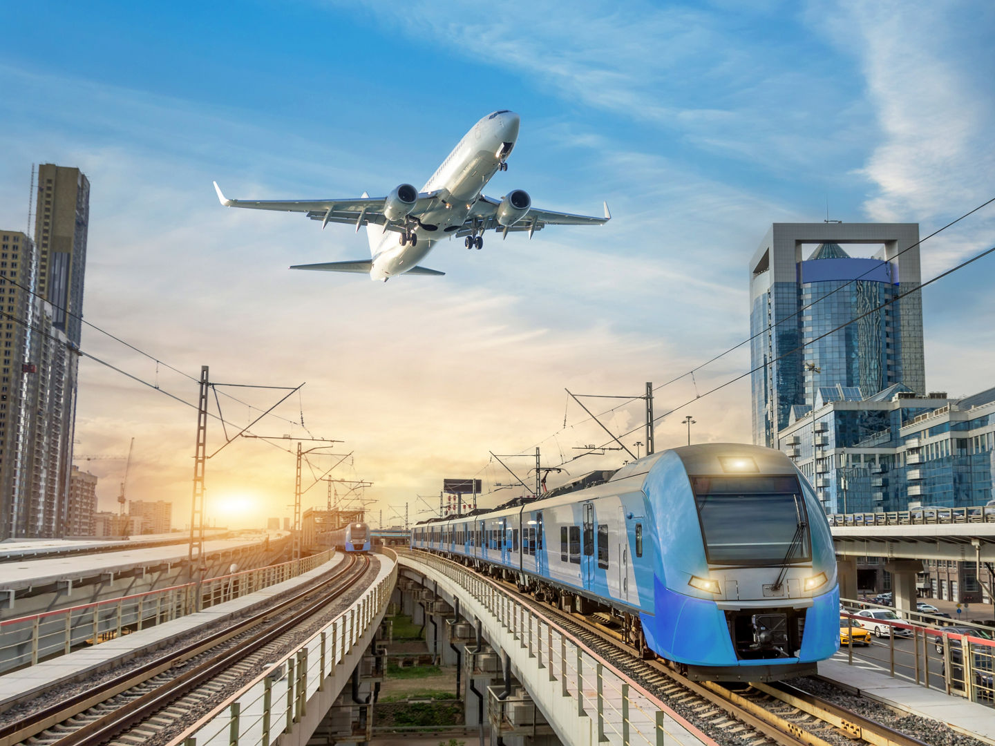Urban view of railway tracks and suburban electric trains rushing along among high rise buildings. Passenger plane flying in sky, landing at airport. Concept of modern infrastructure transport travel