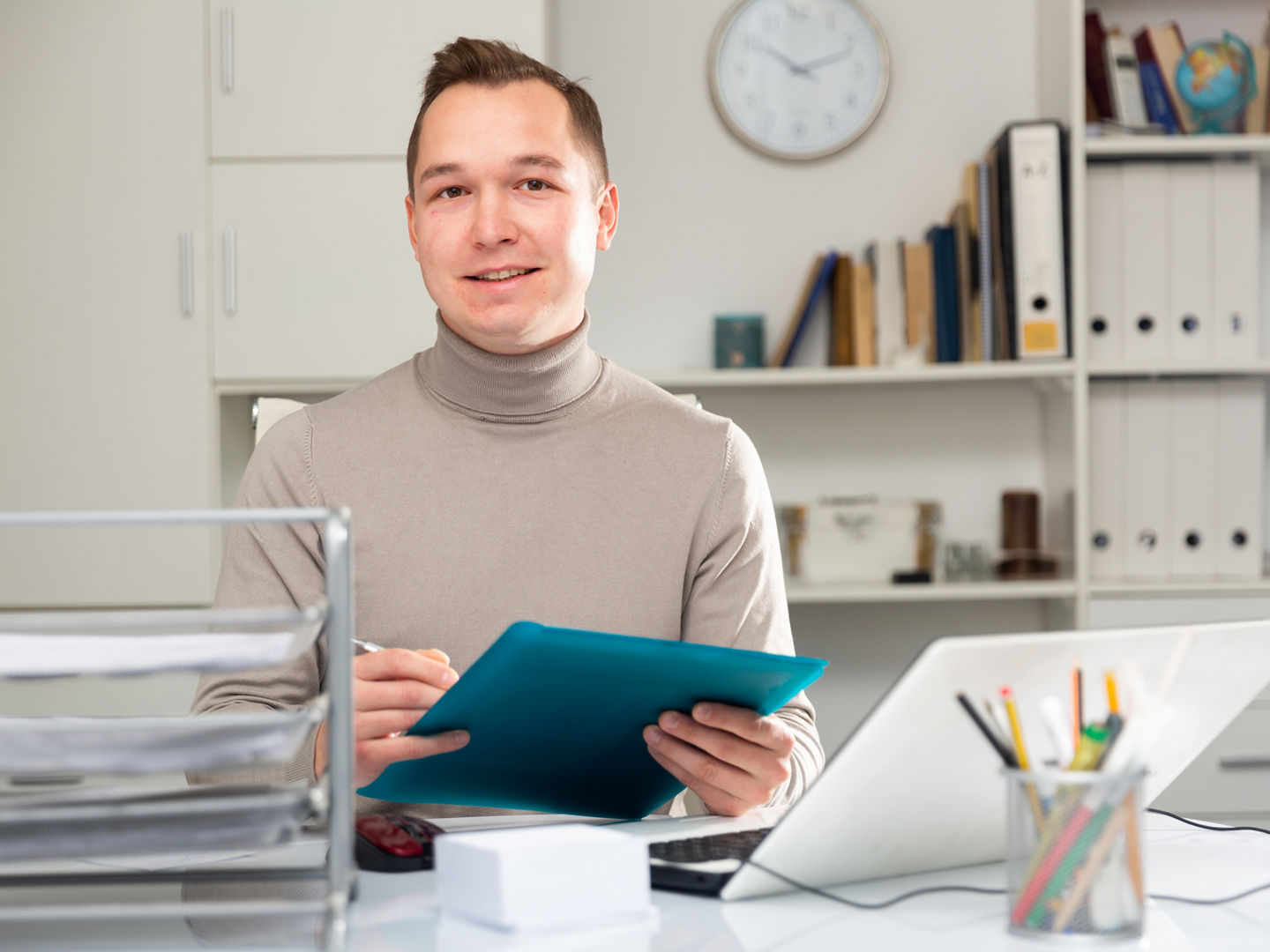 Caucaisan businessman doing his daily work in office. Cheerful man sitting at desk and looking at camera.