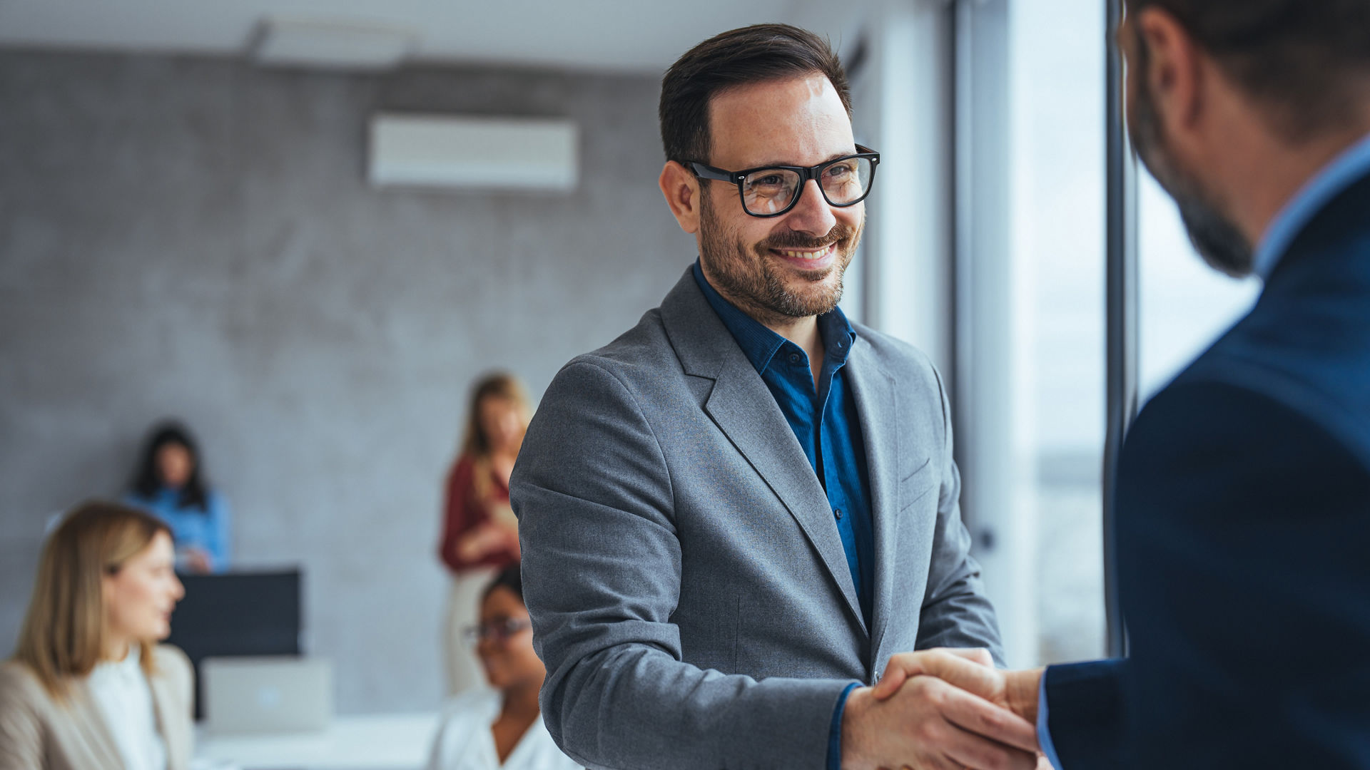 Portrait of cheerful young manager handshake with new employee. Business partnership meeting in office. Close up of handshake in the office. Mature businessman shake hands with a younger colleague