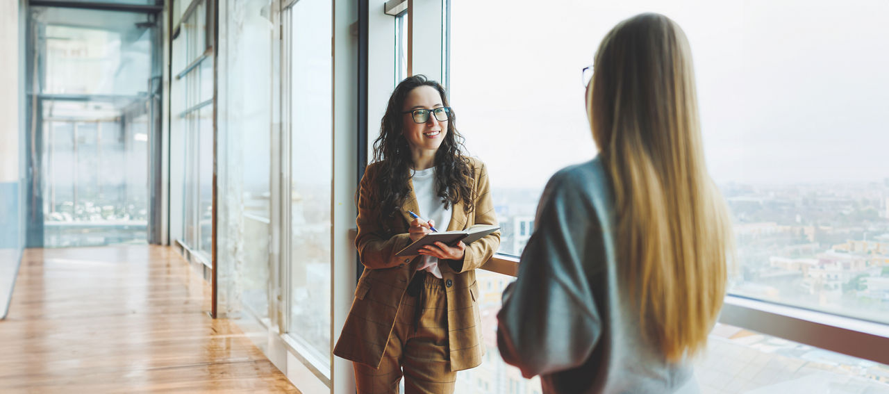 A successful woman in glasses works in the office on the background of colleagues. Modern working day in the office. Businesswoman makes notes in a notebook