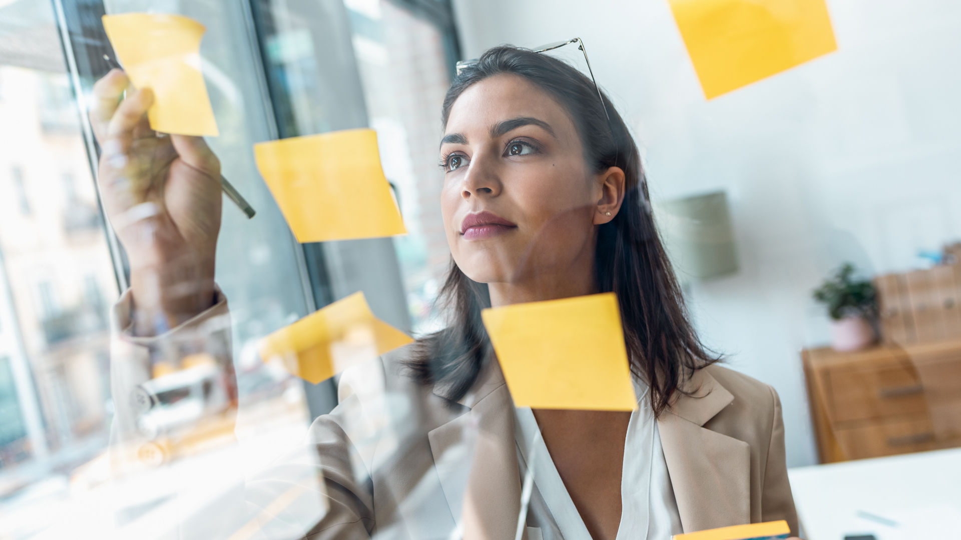 Shot of elegant beautiful businesswoman working on wall glass with post it stickers in the office