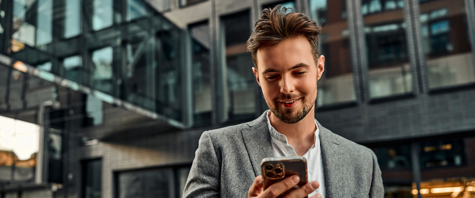 Portrait of an attractive confident modern man holding a phone while making a corporate call. Behind a dark background of lanterns and business buildings. Communication, work online. Copy space.                               