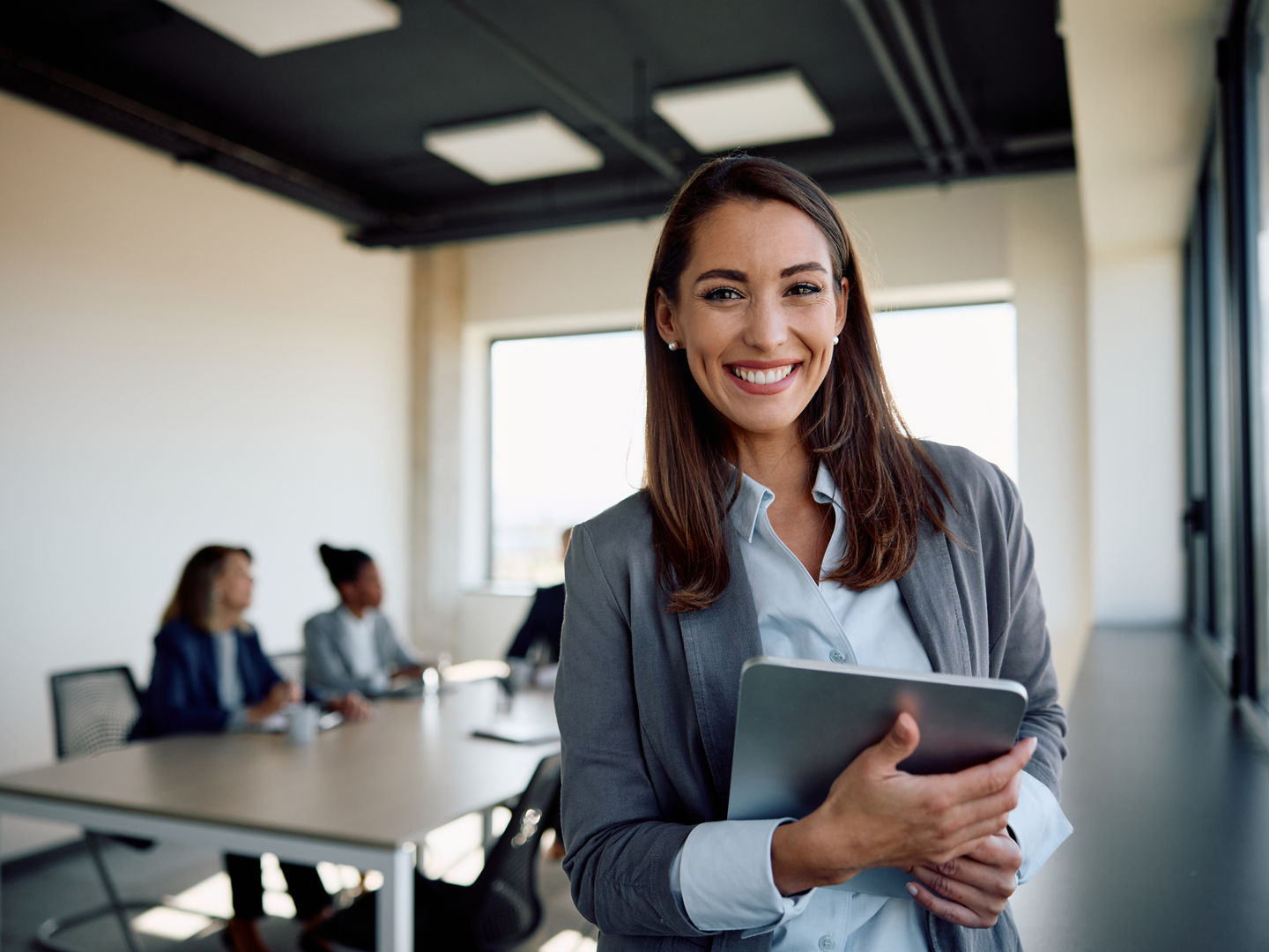 Young happy businesswoman using digital tablet in meeting room and looking at camera.