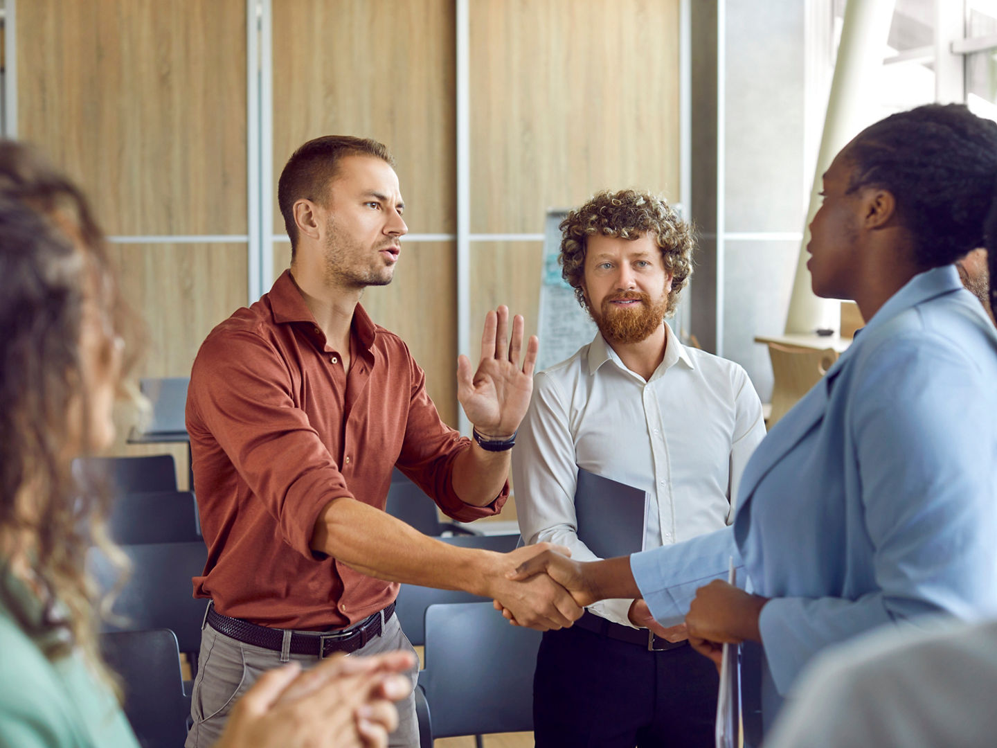 Diverse business people talking and shaking hands greeting each other on meeting in office. Multiracial colleagues employees handshake at briefing with coworkers making a deal and reaching agreement.
