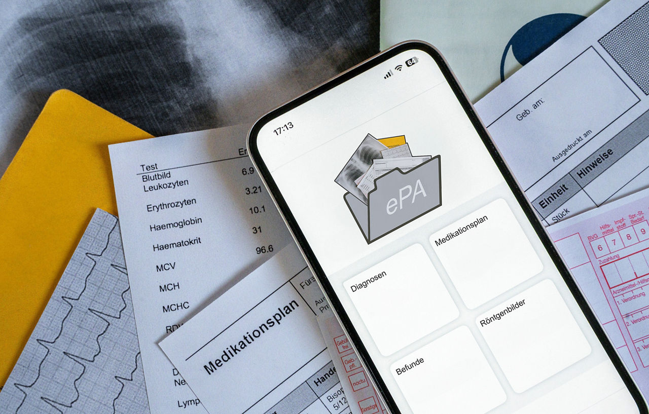 Ein Smartphone auf dem gerade eine elektronische Patientenakte angezeigt wird, liegt auf medizinischen Dokumenten, horizontal