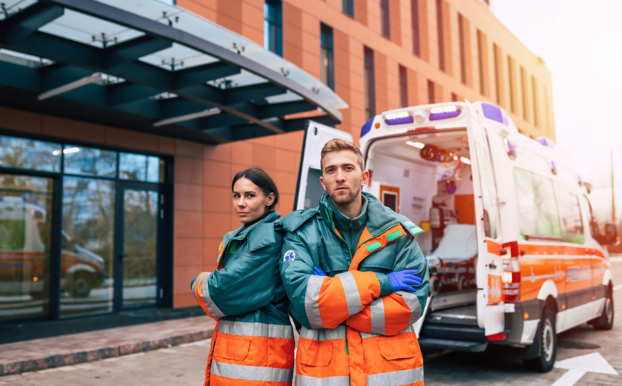 Two confident young doctors looking on the camera on ambulance and hospital background